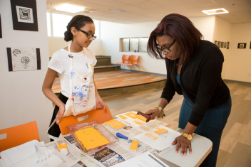 A middle school student watches as a teacher practices a print-making technique she demonstrated for her.
